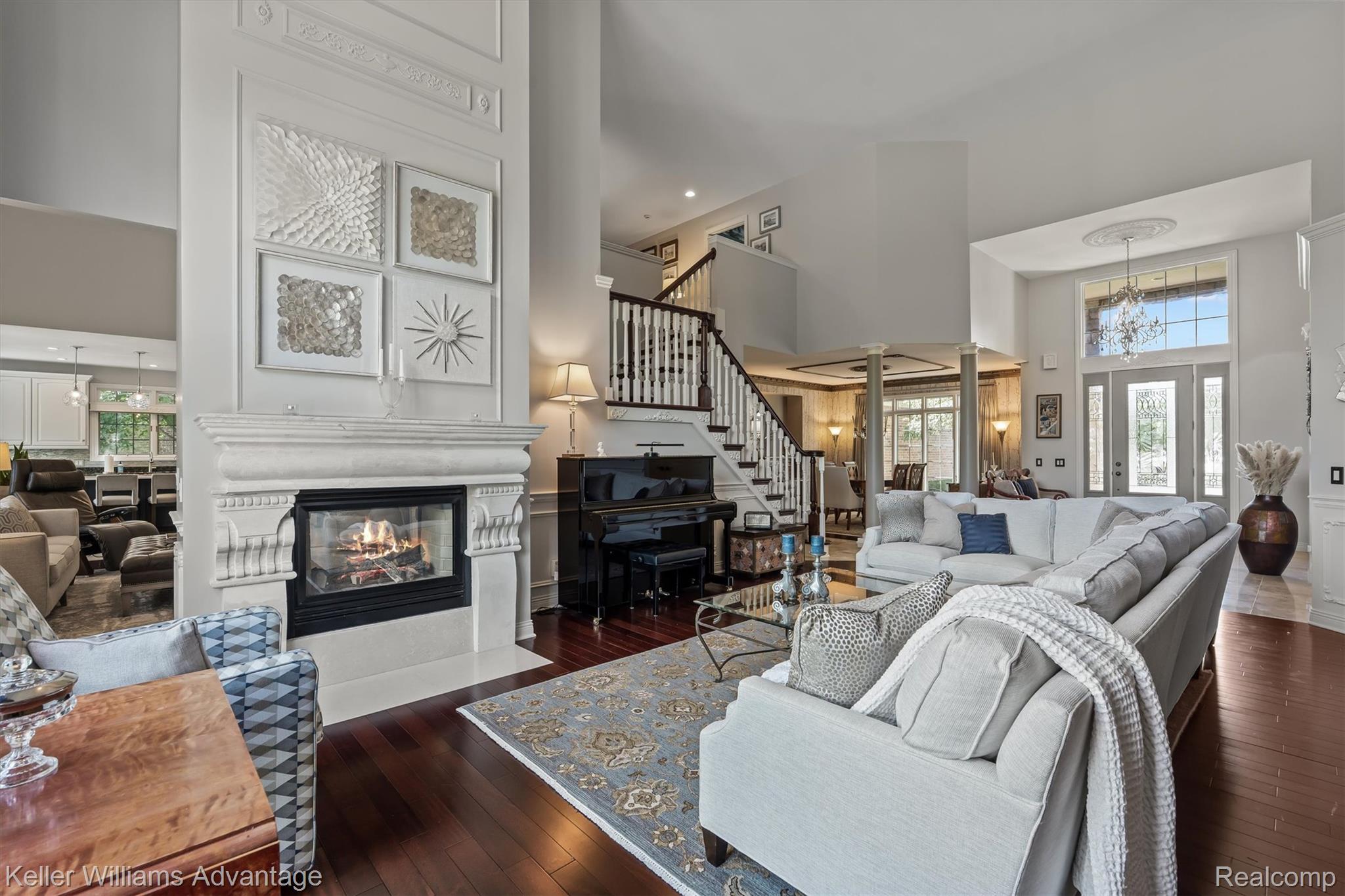 22878 Tree Top Court South Lyon, MI 48178 - Photo 5 of 75 Two-story living area featuring a prominent fireplace with a carved stone mantel, rich wood-finish flooring, and a grand staircase with white balusters