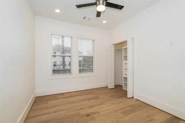 an empty room with wooden floor fan and windows