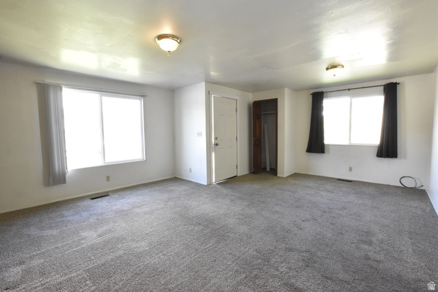 290 West 600 North Logan, UT 84321 - Photo 37 of 45 Spacious room featuring gray carpeting, white walls, two windows with vertical blinds and dark curtains, a white entry door, and a built-in closet with wood-finish trim