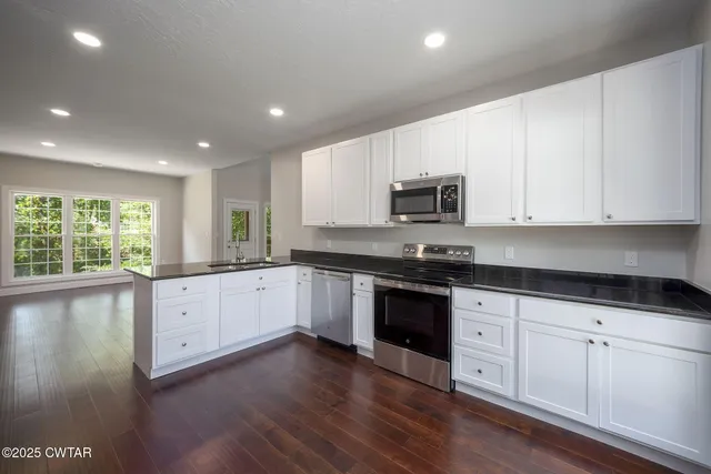 a large kitchen with granite countertop a stove a sink a window and wooden floor