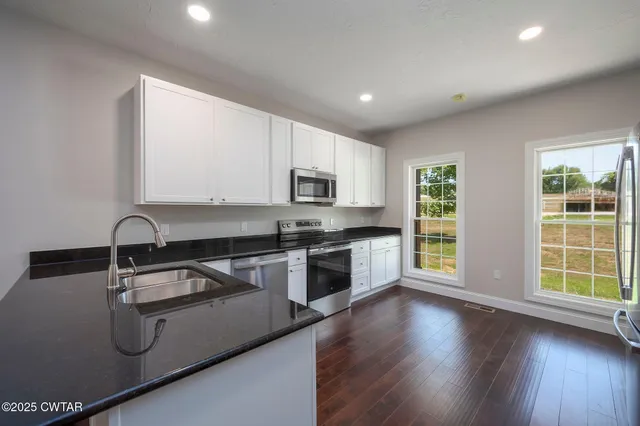 a kitchen with stainless steel appliances granite countertop a stove a sink a refrigerator white cabinets and a wooden floor