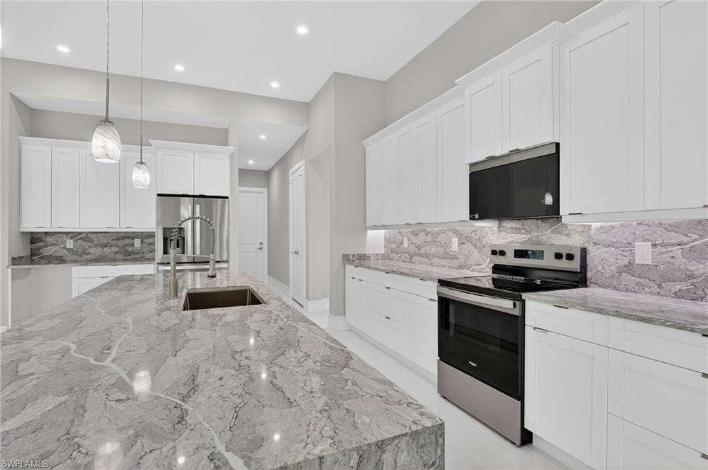 563 15th Street Northwest Naples, FL 34120 - Photo 11 of 33 Kitchen featuring light stone counters, stainless steel appliances, backsplash, white cabinetry, and pendant lighting