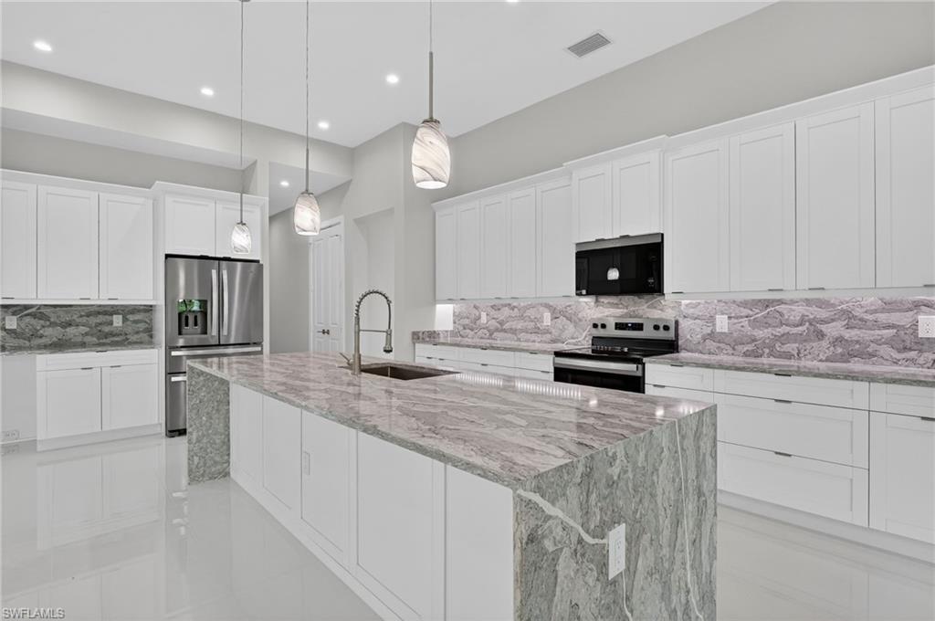 563 15th Street Northwest Naples, FL 34120 - Photo 12 of 33 Kitchen featuring decorative backsplash, white cabinets, light stone countertops, stainless steel appliances, and recessed lighting
