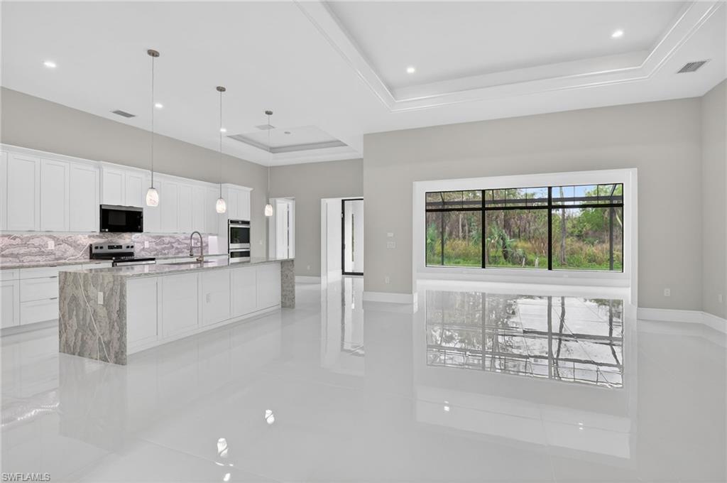 563 15th Street Northwest Naples, FL 34120 - Photo 13 of 33 Kitchen featuring white cabinetry, light stone counters, decorative light fixtures, stainless steel appliances, and a raised ceiling