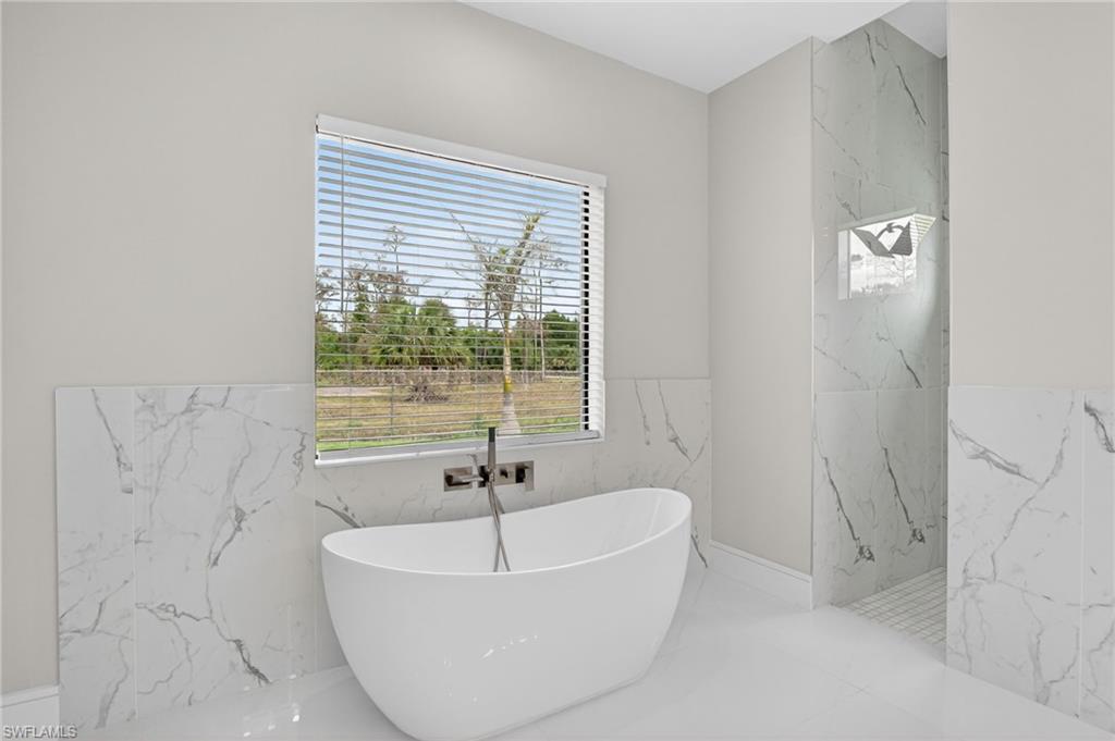 563 15th Street Northwest Naples, FL 34120 - Photo 17 of 33 Bathroom with marble tiled flooring, a soaking tub, and stone wall