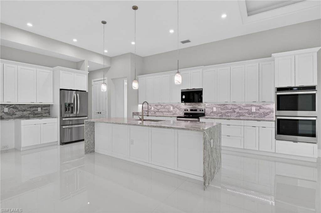 563 15th Street Northwest Naples, FL 34120 - Photo 22 of 33 Kitchen with backsplash, light stone counters, white cabinets, and recessed lighting