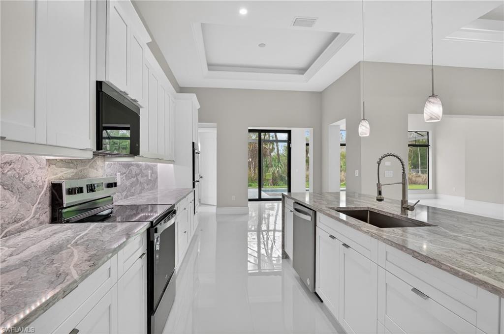 563 15th Street Northwest Naples, FL 34120 - Photo 23 of 33 Kitchen with stainless steel appliances, white cabinetry, a raised ceiling, light stone counters, and pendant lighting