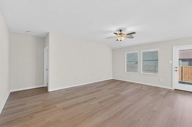a view of an empty room with wooden floor and a ceiling fan