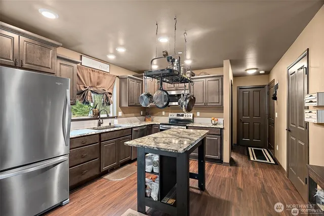 a kitchen with granite countertop a refrigerator a sink a stove and chairs with wooden floor