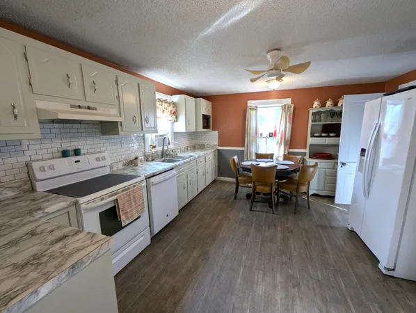 a large white kitchen with stainless steel appliances granite countertop a stove a sink dishwasher and white cabinets with wooden floor