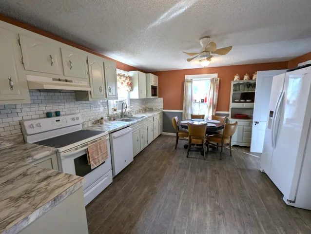 a large white kitchen with stainless steel appliances granite countertop a stove a sink dishwasher and white cabinets with wooden floor