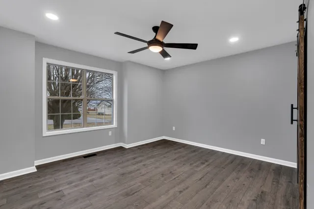an empty room with wooden floor ceiling fan and windows