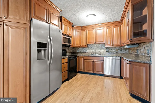 a kitchen with stainless steel appliances granite countertop a refrigerator a sink dishwasher a stove and white countertops with wooden floor