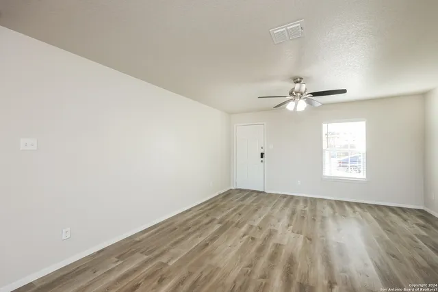 an empty room with wooden floor fan and windows