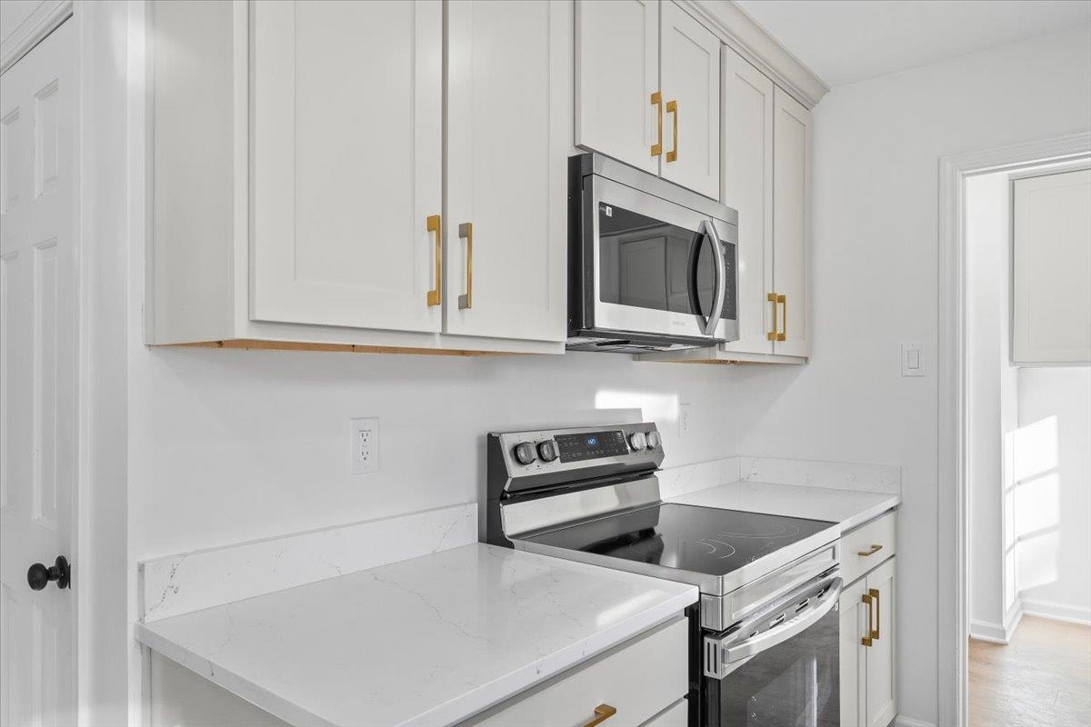 1676 Miller Farms Road Germantown, TN 38138 - Photo 15 of 37 Kitchen featuring white cabinetry with gold-toned hardware, white countertops, stainless steel microwave, and a black electric range
