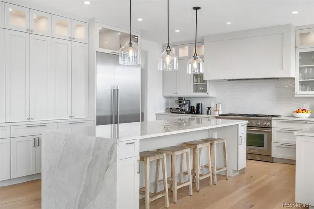 a kitchen with kitchen island granite countertop a stove a sink a refrigerator and white cabinets with wooden floor