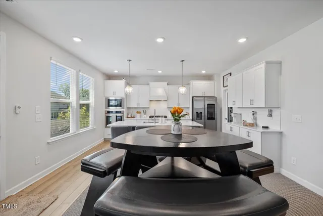 a kitchen with stainless steel appliances a dining table chairs stove refrigerator and cabinets