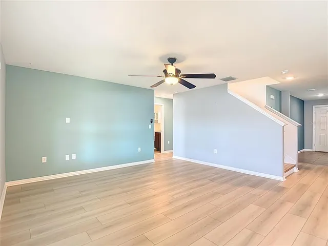 an empty room with wooden floor chandelier fan and windows