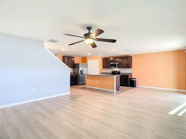 a view of an empty room with wooden floor and a ceiling fan