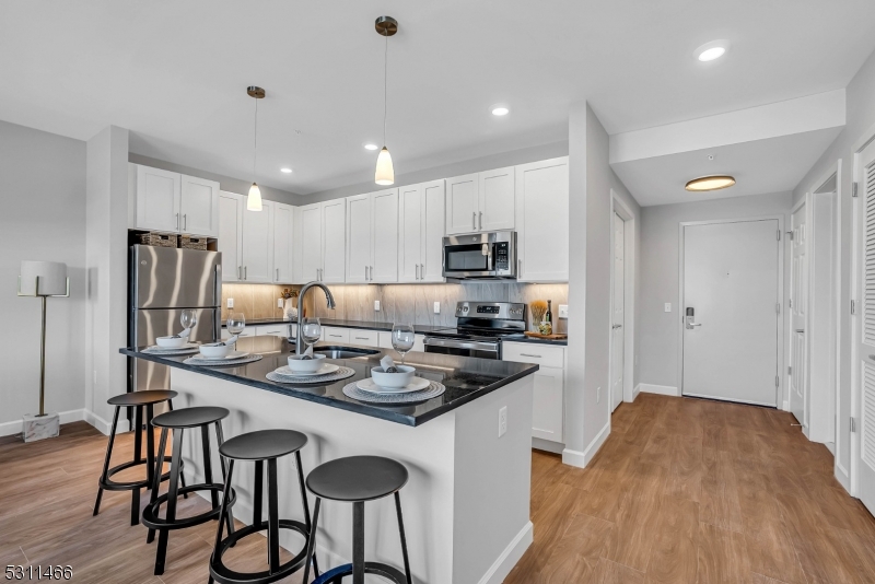 a kitchen with stainless steel appliances granite countertop a stove a refrigerator a sink a dining table and chairs with wooden floor