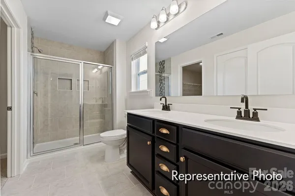 a spacious bathroom with a double vanity sink a toilet a mirror and shower