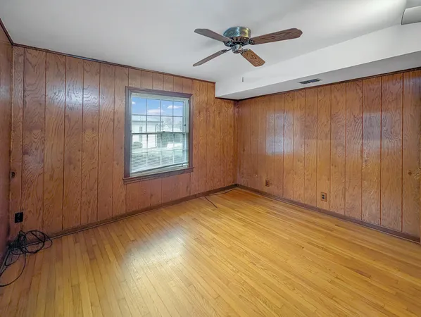 an empty room with wooden floor chandelier fan and windows