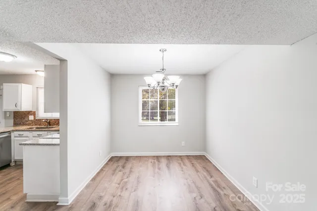 an empty room with wooden floor chandeliers and kitchen view