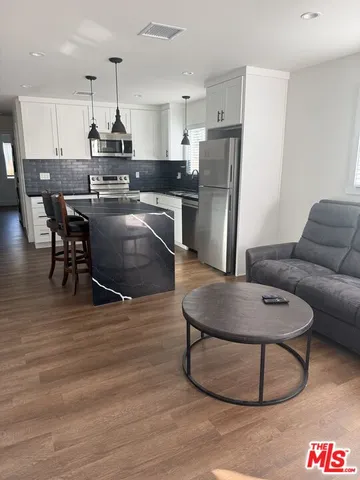 a kitchen with stainless steel appliances granite countertop a refrigerator a stove a sink a dining table and chairs with wooden floor