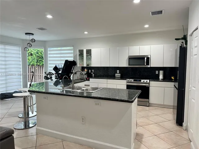 a kitchen with kitchen island granite countertop a sink a counter top space appliances and cabinets