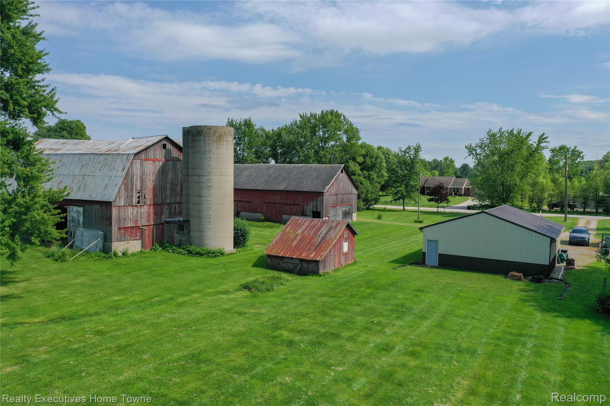 8728 Rynn Road Avoca, MI 48006 - Photo 49 of 53 Expansive green lawn featuring multiple outbuildings, including a large red barn with a metal roof, a concrete silo, a smaller red outbuilding with a rusted metal roof, and a light-colored metal building with a dark trim and a dark roof