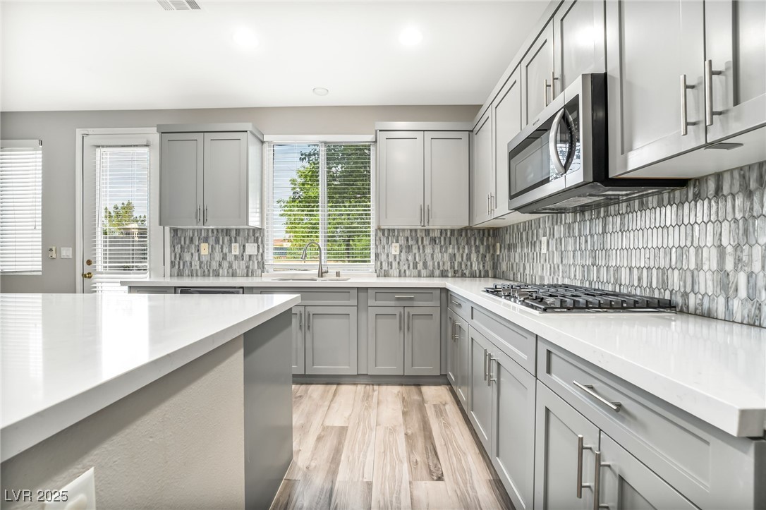1533 Sabatini Drive Henderson, NV 89052 - Photo 8 of 27 Kitchen with gray cabinets, backsplash, light wood-style floors, recessed lighting, and light stone counters