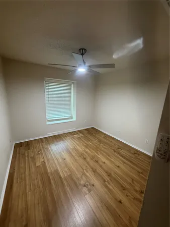 an empty room with wooden floor fan and windows
