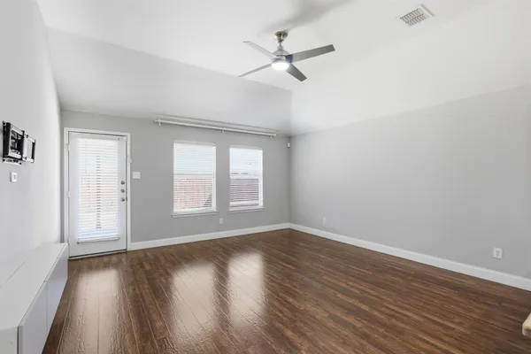 an empty room with wooden floor fan and windows