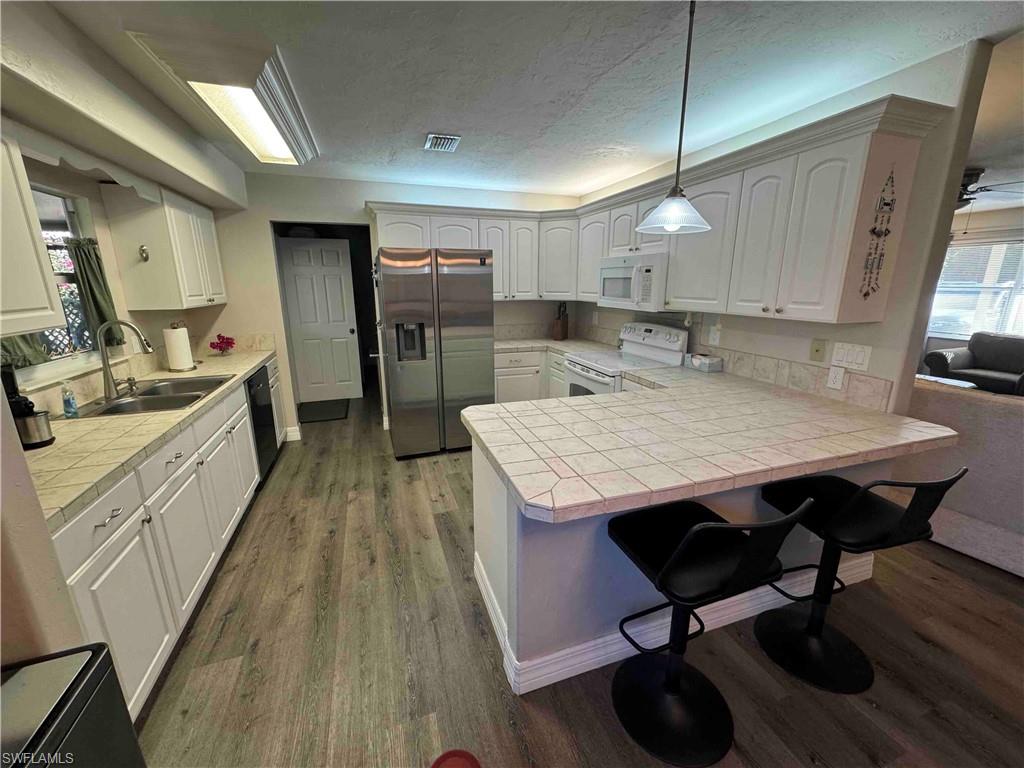 203 Esther Street Naples, FL 34104 - Photo 11 of 33 Kitchen featuring white appliances, tile counters, white cabinets, a textured ceiling, and dark wood finished floors