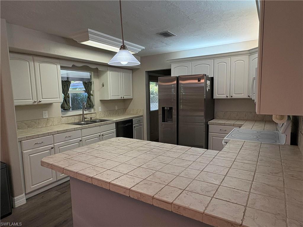 203 Esther Street Naples, FL 34104 - Photo 9 of 33 Kitchen featuring a peninsula, stainless steel refrigerator with ice dispenser, decorative light fixtures, white electric range, and white cabinets