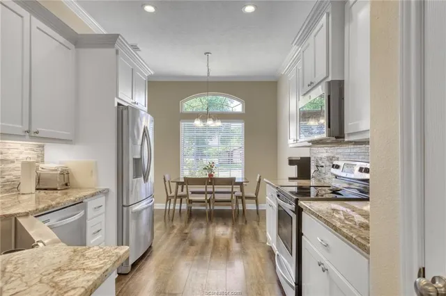 a kitchen with stainless steel appliances a stove a sink dishwasher a refrigerator white cabinets and wooden floor next to a window