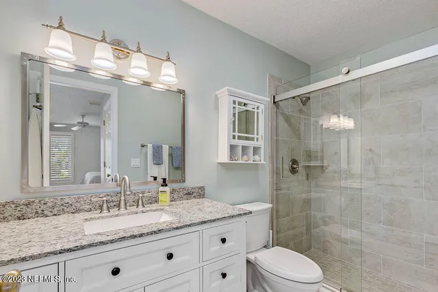 a bathroom with a granite countertop sink a toilet a mirror and shower