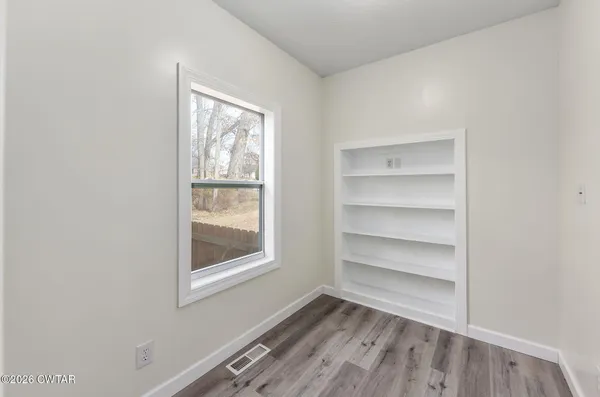a view of an empty room with a window and wooden floor