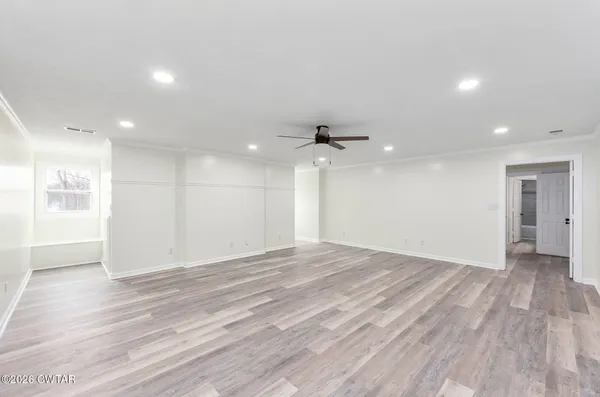 a view of an empty room with wooden floor kitchen and a window