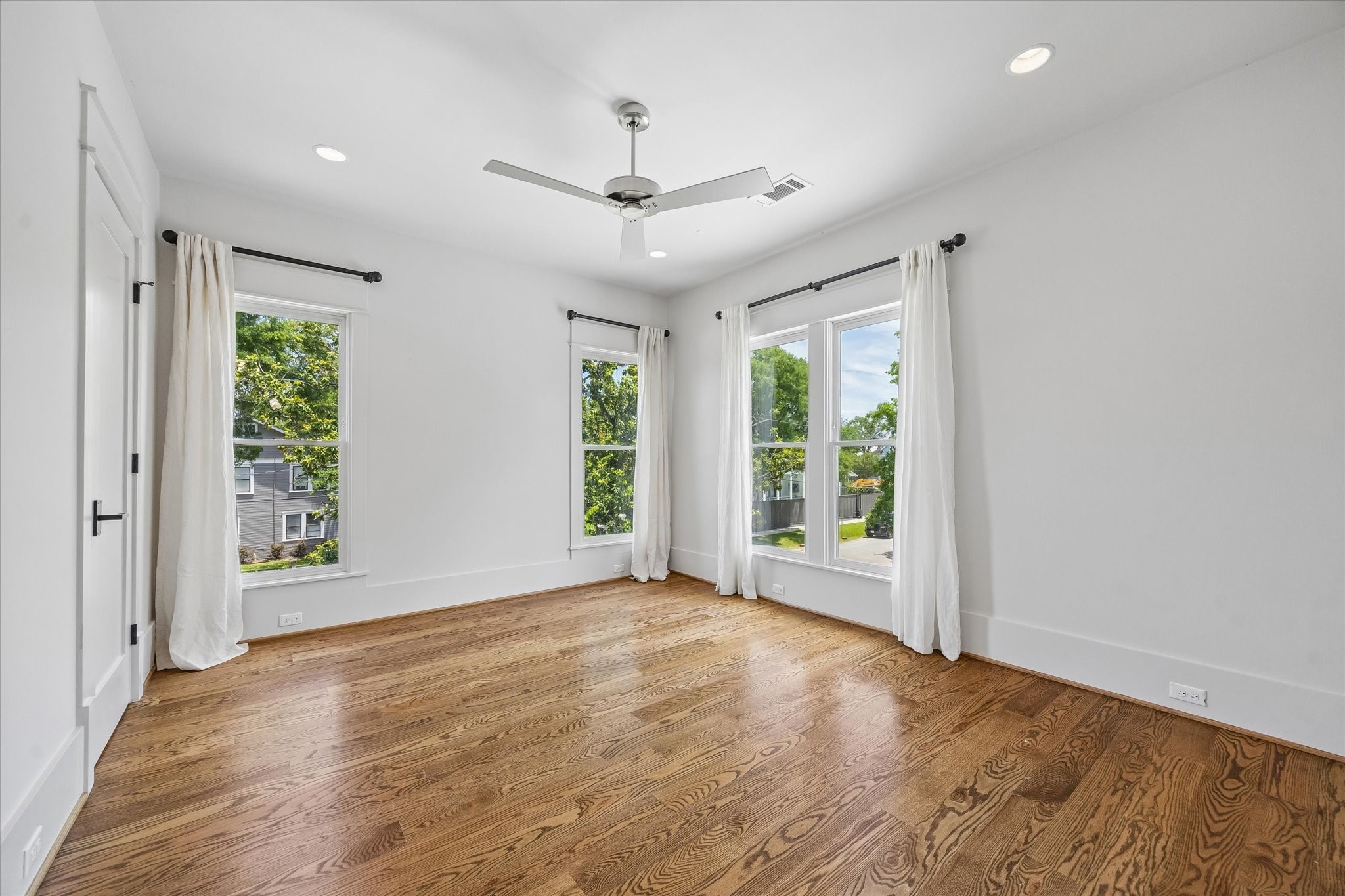 1101 Omar Street Houston, TX 77009 - Photo 27 of 46 Second bedroom features hardwood floors, large windows with white curtains offering abundant natural light, and a modern ceiling fan, creating a bright and airy space.