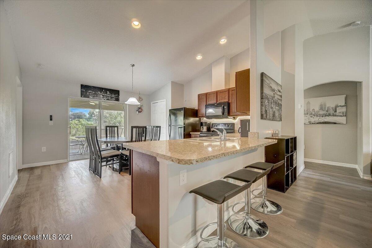 1459 Saxony Road Southwest Palm Bay, FL 32908 - Photo 9 of 38 a kitchen with stainless steel appliances kitchen island granite countertop a refrigerator a stove a sink a dining table and chairs with wooden floor