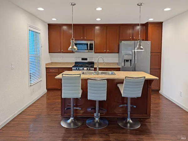 a kitchen with stainless steel appliances granite countertop a stove top oven a refrigerator a kitchen island with chairs and wooden floor
