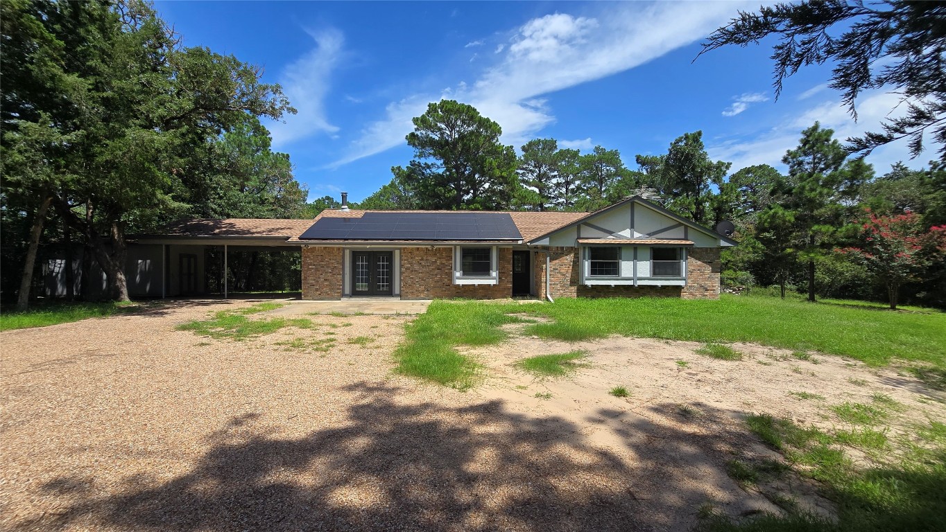 View of front facade with roof mounted solar panels, french doors, a carport, brick siding, and dirt driveway