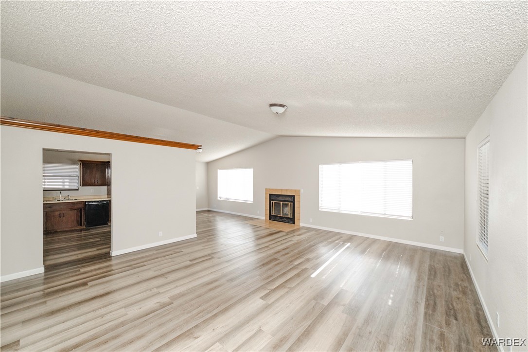 2063 East Sundown Road Kingman, AZ 86409 - Photo 11 of 40 Unfurnished living room with vaulted ceiling, a tile fireplace, a textured ceiling, baseboards, and light wood-style floors