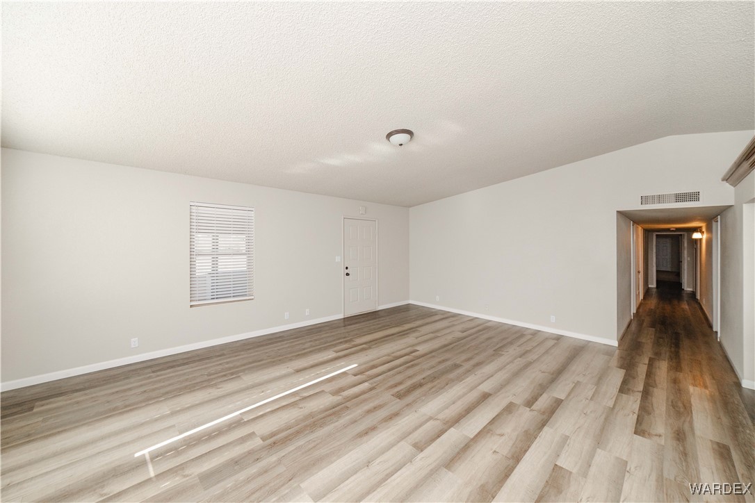 2063 East Sundown Road Kingman, AZ 86409 - Photo 13 of 40 Empty room with a textured ceiling, light wood-style floors, lofted ceiling, and visible vents
