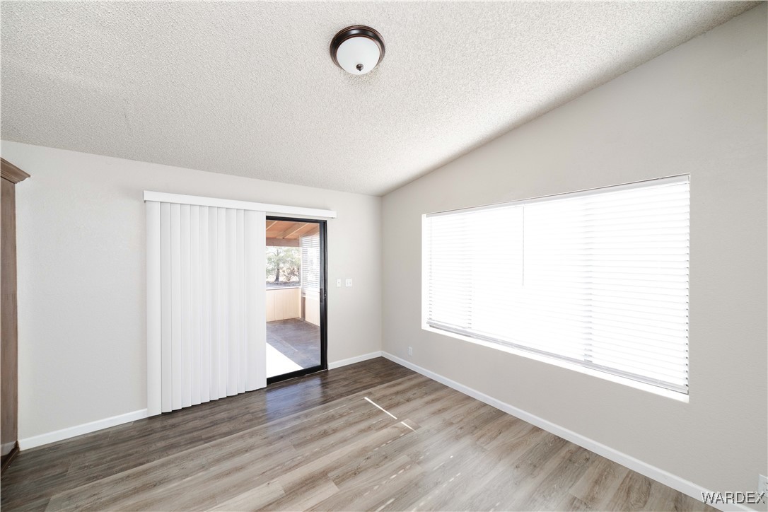 2063 East Sundown Road Kingman, AZ 86409 - Photo 15 of 40 Unfurnished bedroom with baseboards, lofted ceiling, wood finished floors, and a textured ceiling