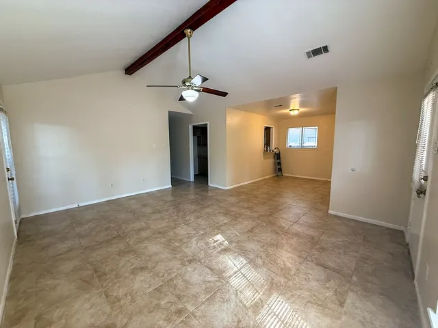 an empty room with chandelier fan and windows