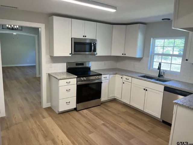 a kitchen with stainless steel appliances white cabinets a sink a stove a microwave and wooden floors