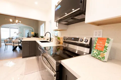 a kitchen with stainless steel appliances a sink a stove top oven a chimney and a dining table with wooden floor