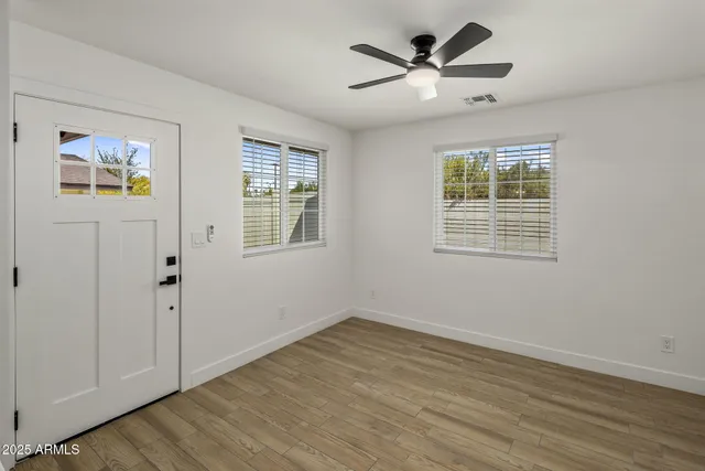 a view of an empty room with wooden floor and a ceiling fan